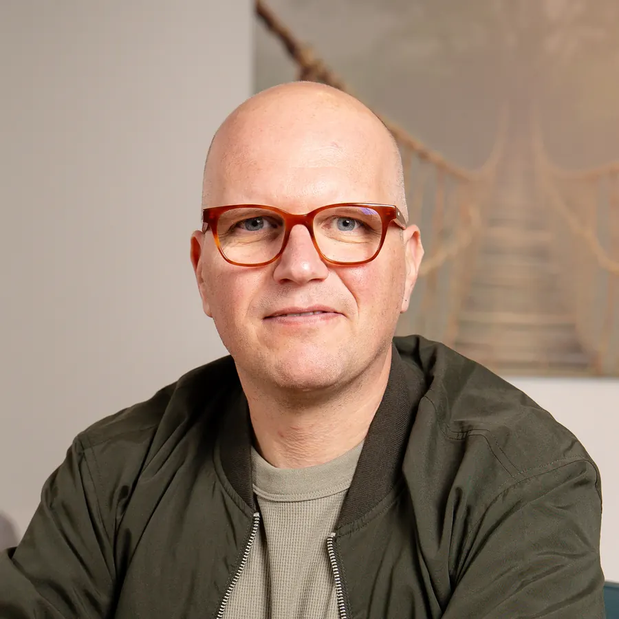 Jan Jacobs aan tafel in zijn praktijk in Mechelen, met het schilderij van de hangbrug achter hem