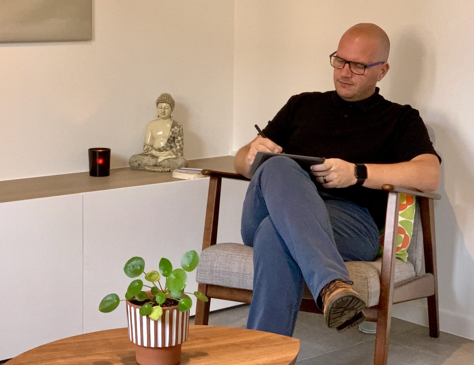 Jan Jacobs in een houten zetel in zijn praktijk in Mechelen, met een notitieboek op zijn knie