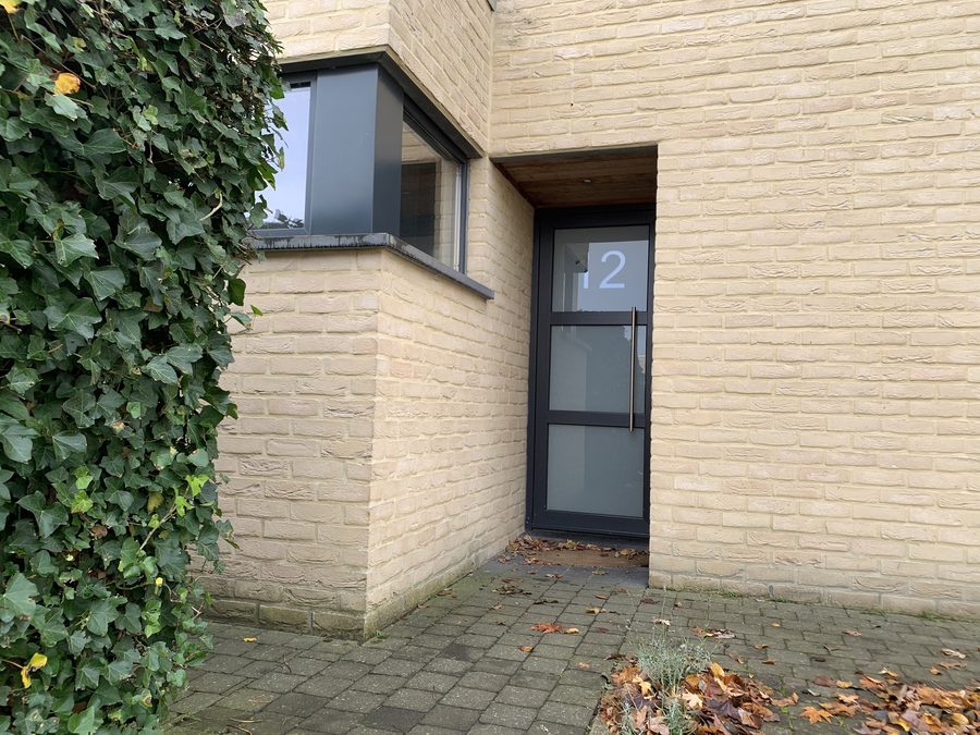 De voordeur van nummer 12, in een gevel van lichte baksteen met klimop ernaast